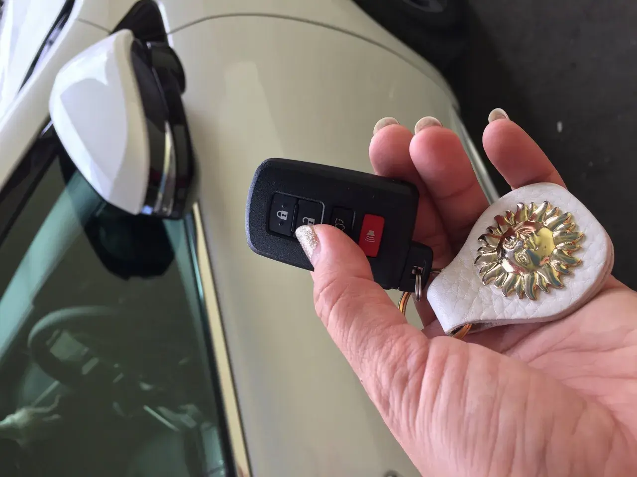 Uszkodzony transponder w kluczyku objawy: auto nie odpala, miga kontrolka. Dłoń trzyma kluczyk z breloczkiem w kształcie słońca.