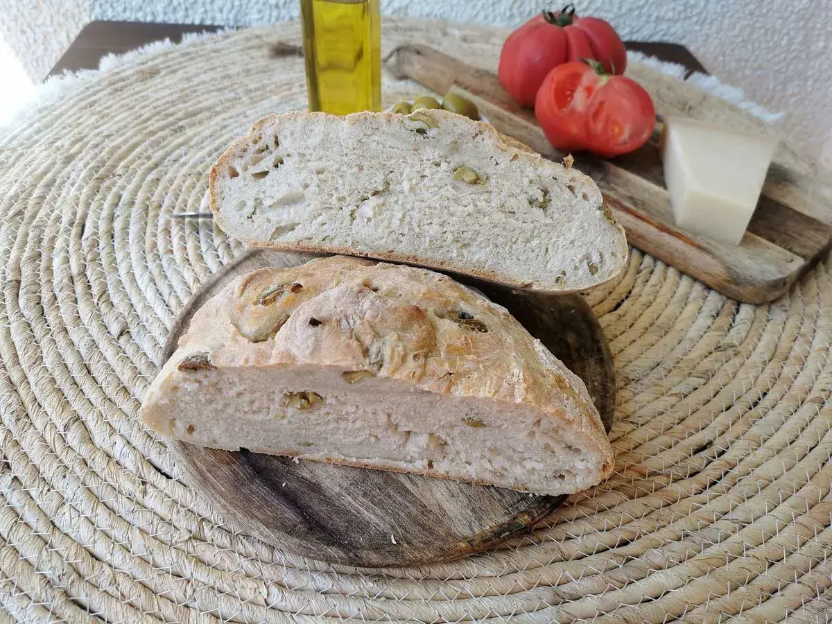 Pan rústico con aceitunas, tomates, queso y aceite de oliva. Un delicioso pan de aceitunas listo para disfrutar.