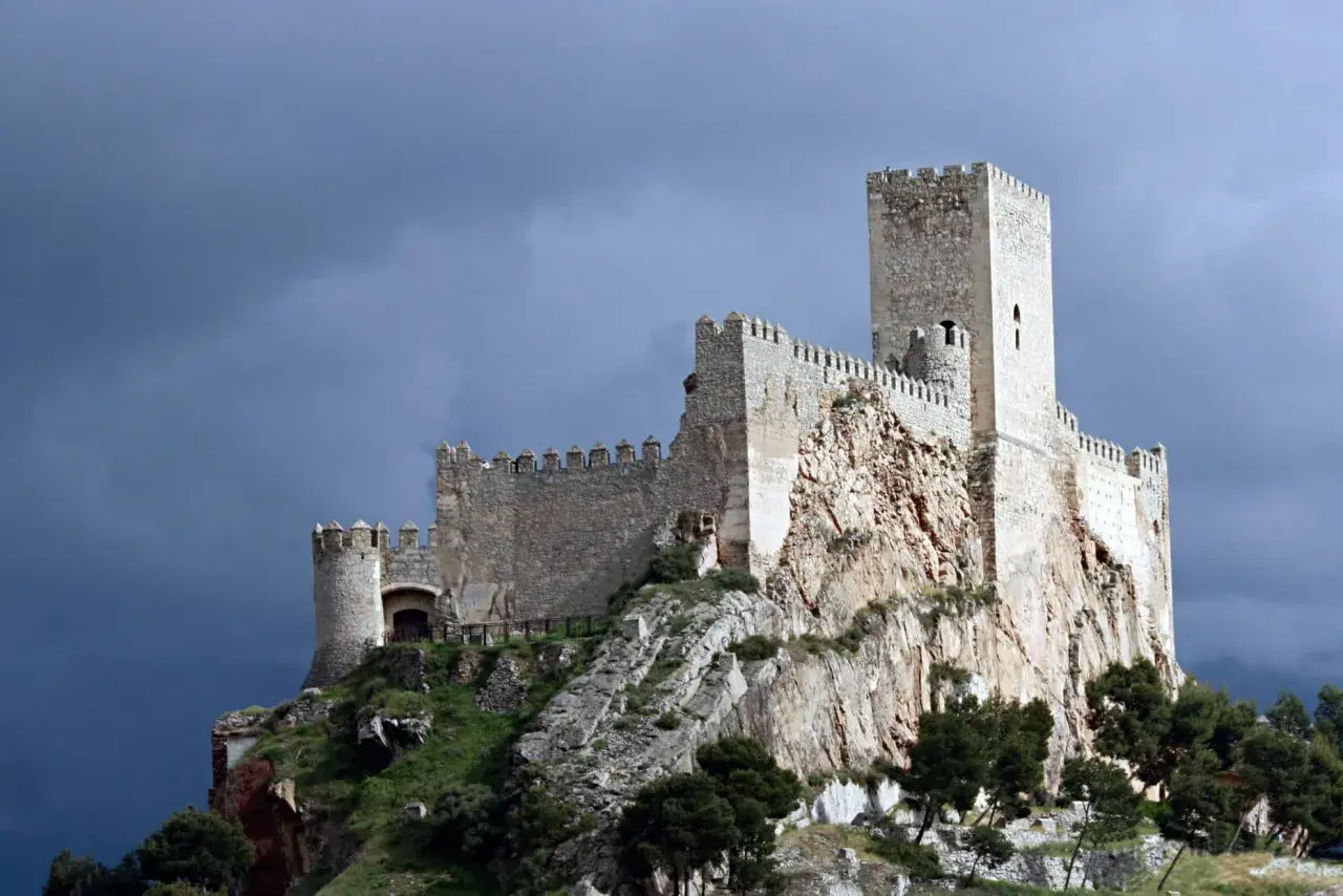 Castillo medieval en lo alto de un peñasco, parte de la ruta de la lana, bajo un cielo tormentoso.