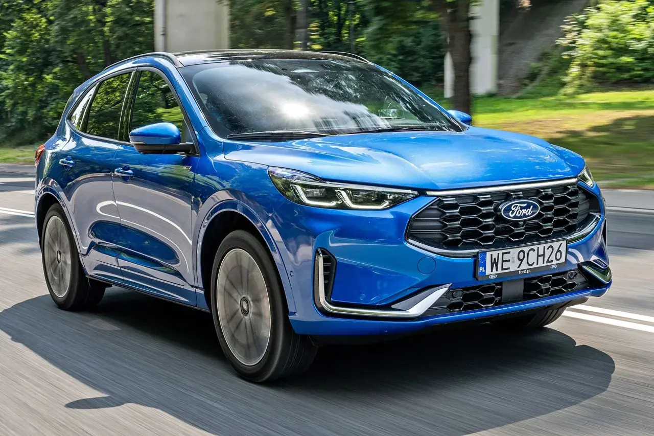 Niebieski Ford Kuga 2025 pędzi po drodze, otoczony zielenią.