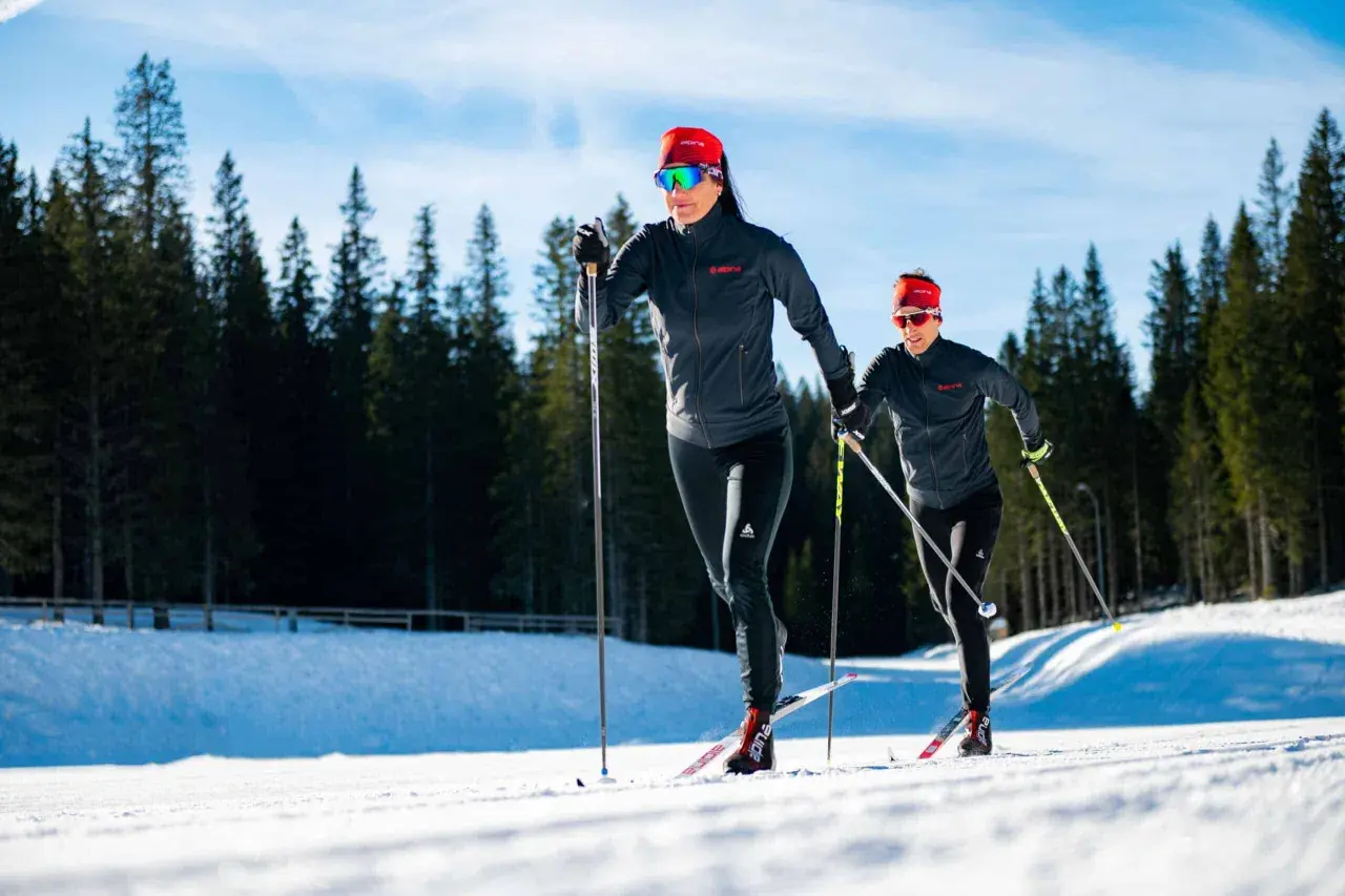 Dwie kobiety w sportowych strojach pokonują trasę narciarską. Długość nart biegowych jest kluczowa dla ich szybkości i stabilności na śniegu.