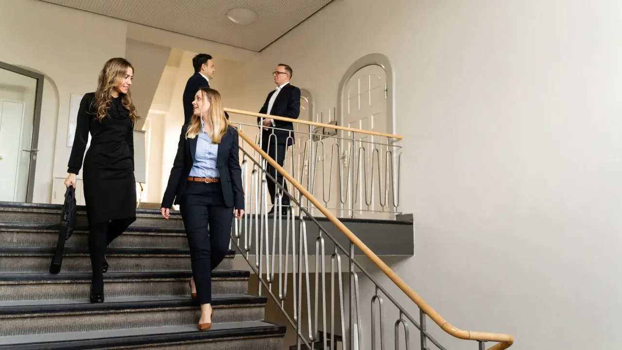 Zwei Frauen und zwei Männer in Business-Kleidung gehen eine Treppe hinunter. Sie könnten sich auf dem Weg zu einem LLM-Kurs berufsbegleitend befinden.