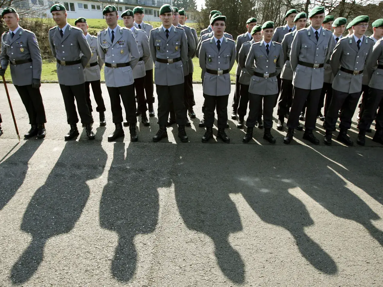 Soldaten der Bundeswehr in Uniform mit grünen Baretts stehen Spalier. Ihre Schatten werfen lange Linien auf den Asphalt.