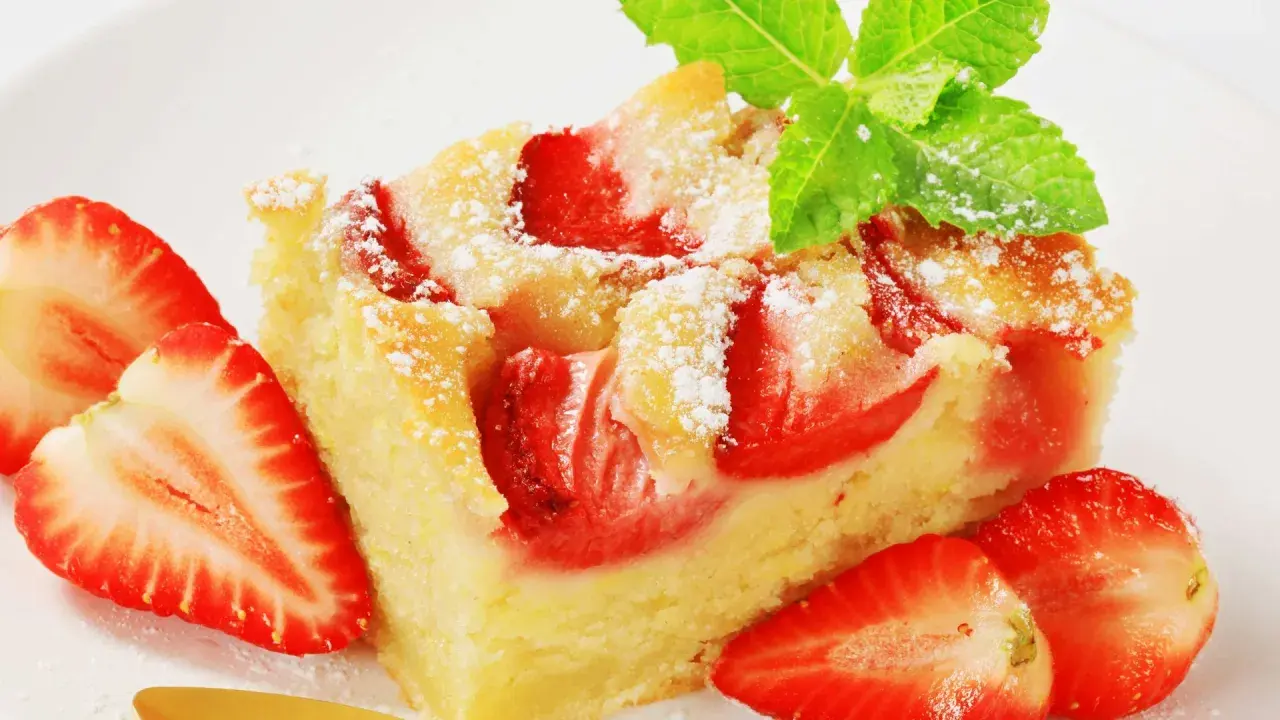 Ein saftiger Erdbeer Blechkuchen, bestäubt mit Puderzucker und garniert mit frischen Erdbeeren und Minze.