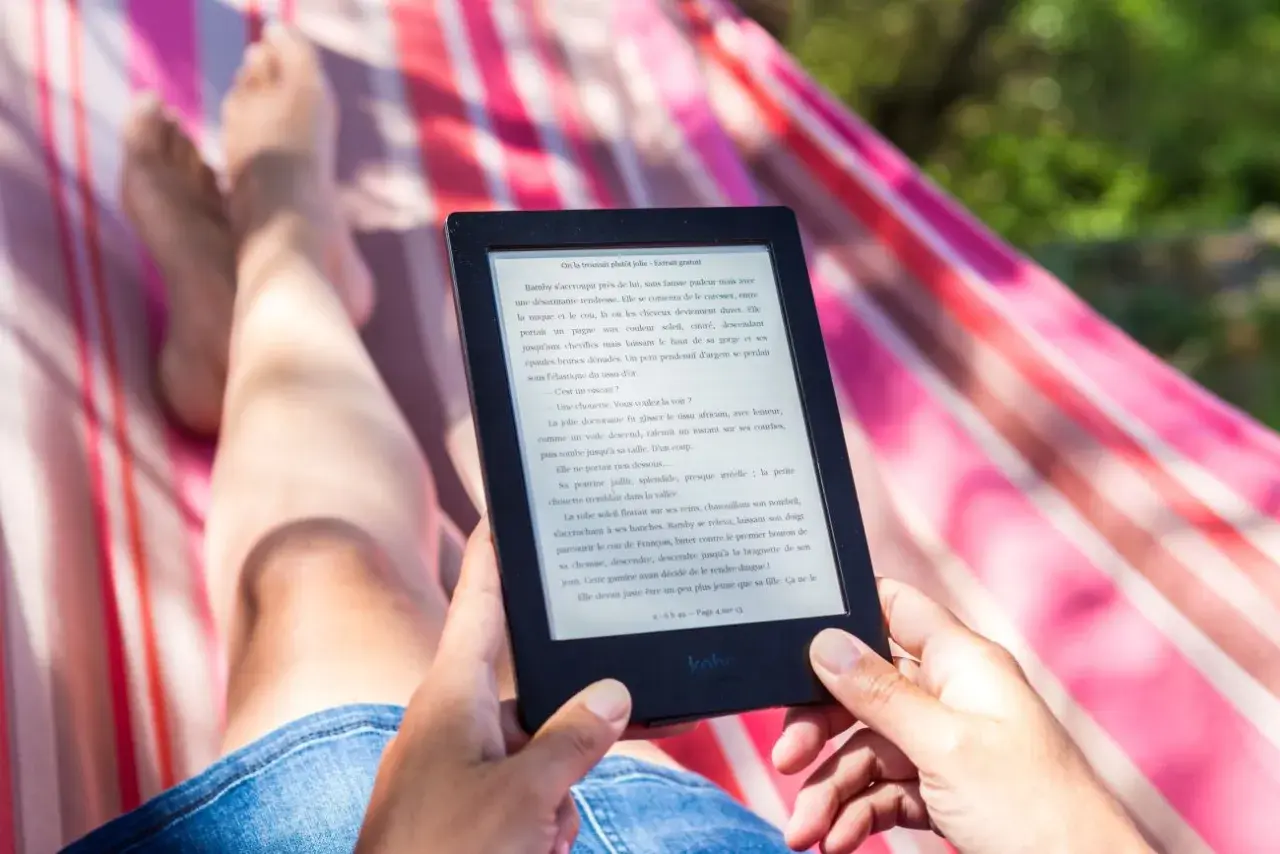 Osoba relaksuje się w hamaku, czytając e-booka. Idealny sposób na wakacje, gdy szukasz najlepszego czytnik ebook ranking.