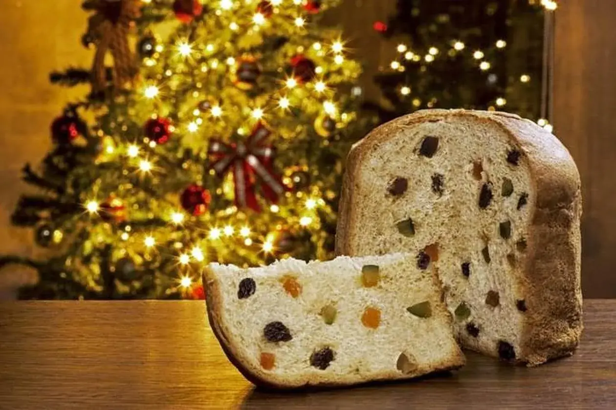Un panettone, symbole de Noël, avec sa tranche coupée révélant fruits confits et raisins secs. Son origine italienne se célèbre devant un sapin illuminé.