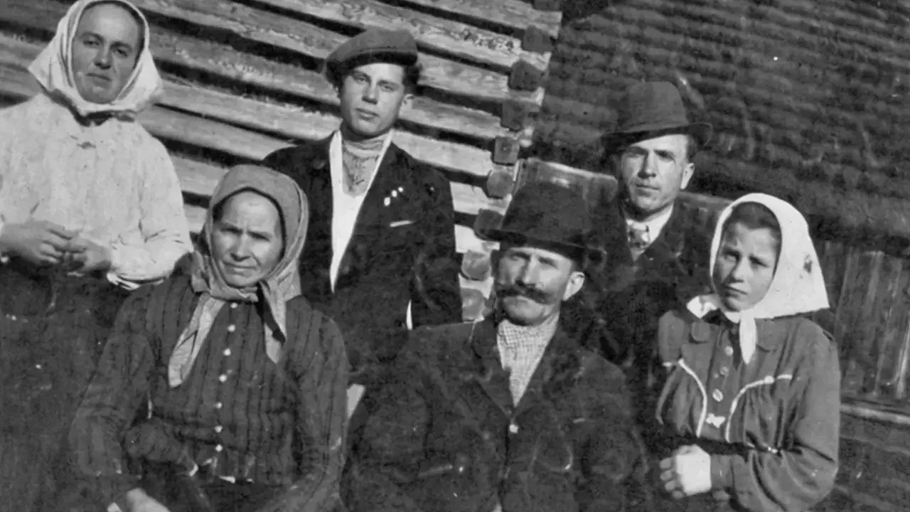 Famille posant devant une maison en bois. Les femmes portent des foulards, les hommes des chapeaux. Un nom de famille slovaque pourrait être associé à cette photo d'ancêtres.