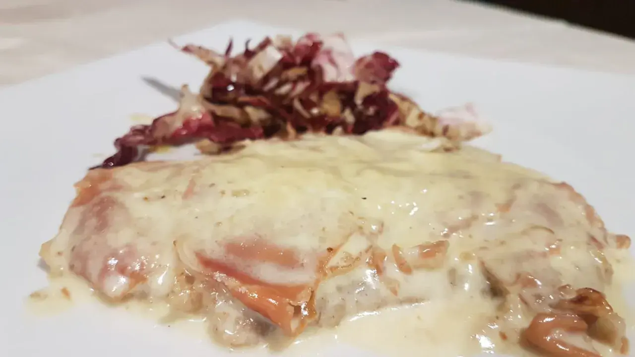 Deliziosa cotoletta alla bolognese, dorata e ricoperta da una cremosa salsa, accompagnata da radicchio croccante.