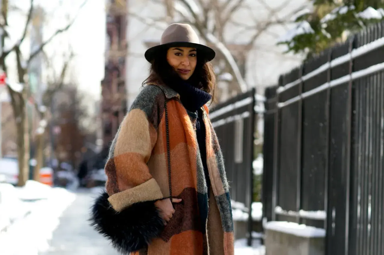 Une femme élégante avec un manteau coloré, un chapeau et un sac en fourrure, parfaite pour savoir comment s'habiller en hiver femme.