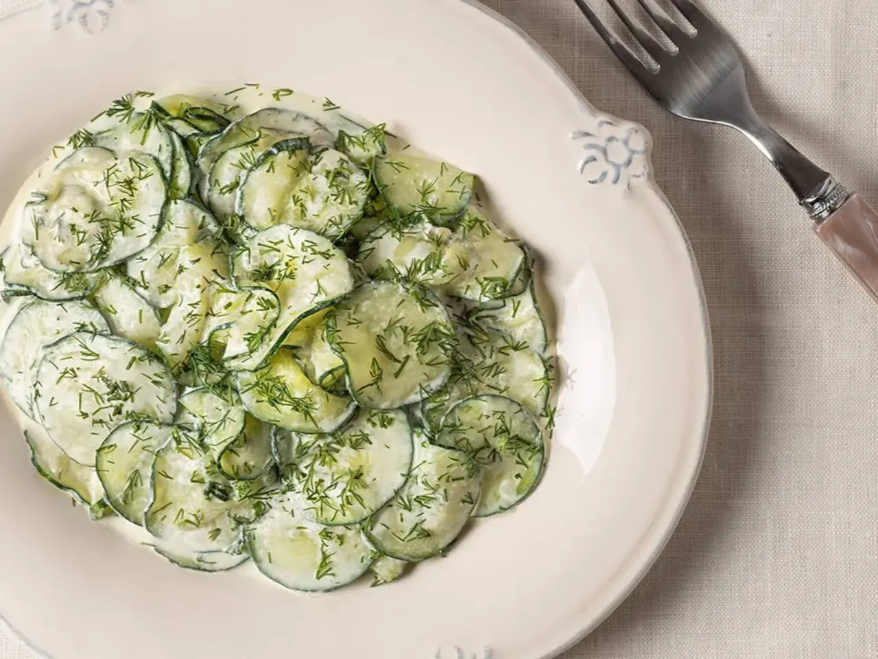 Ensalada alemana de pepino en rodajas finas, cubierta con una cremosa salsa y eneldo fresco, servida en un plato blanco.