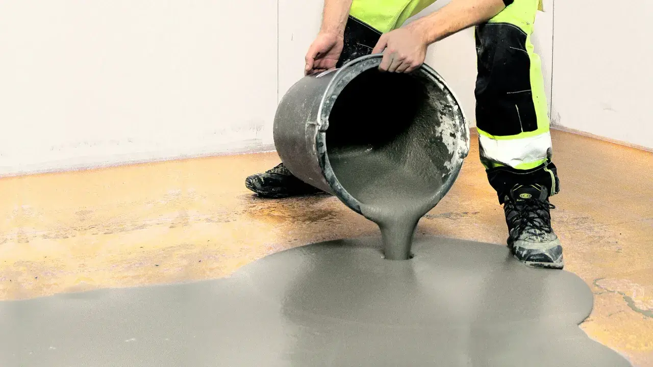 Arbetare häller jordfuktad betong från en hink för att jämna ut ett golv.