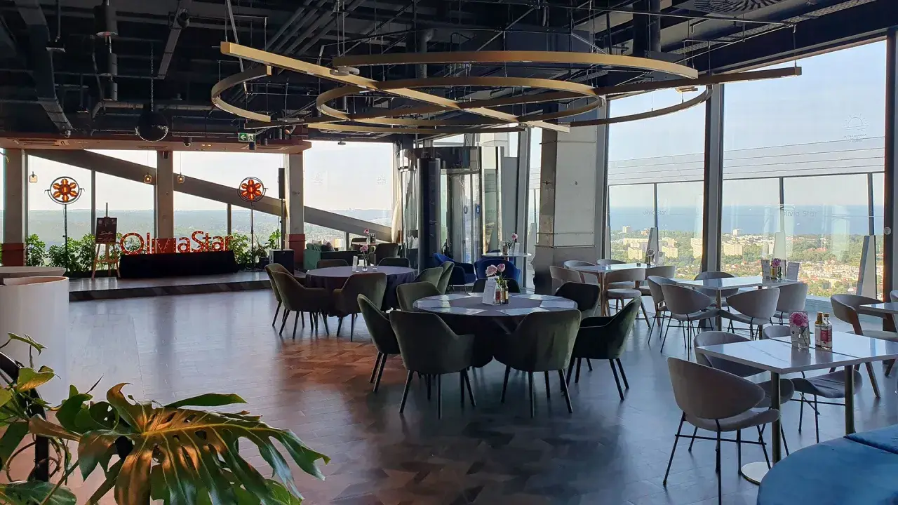 Eleganckie wnętrze restauracji Olivia Star z widokiem na miasto i morze. Stoły nakryte, gotowe na przyjęcie gości.