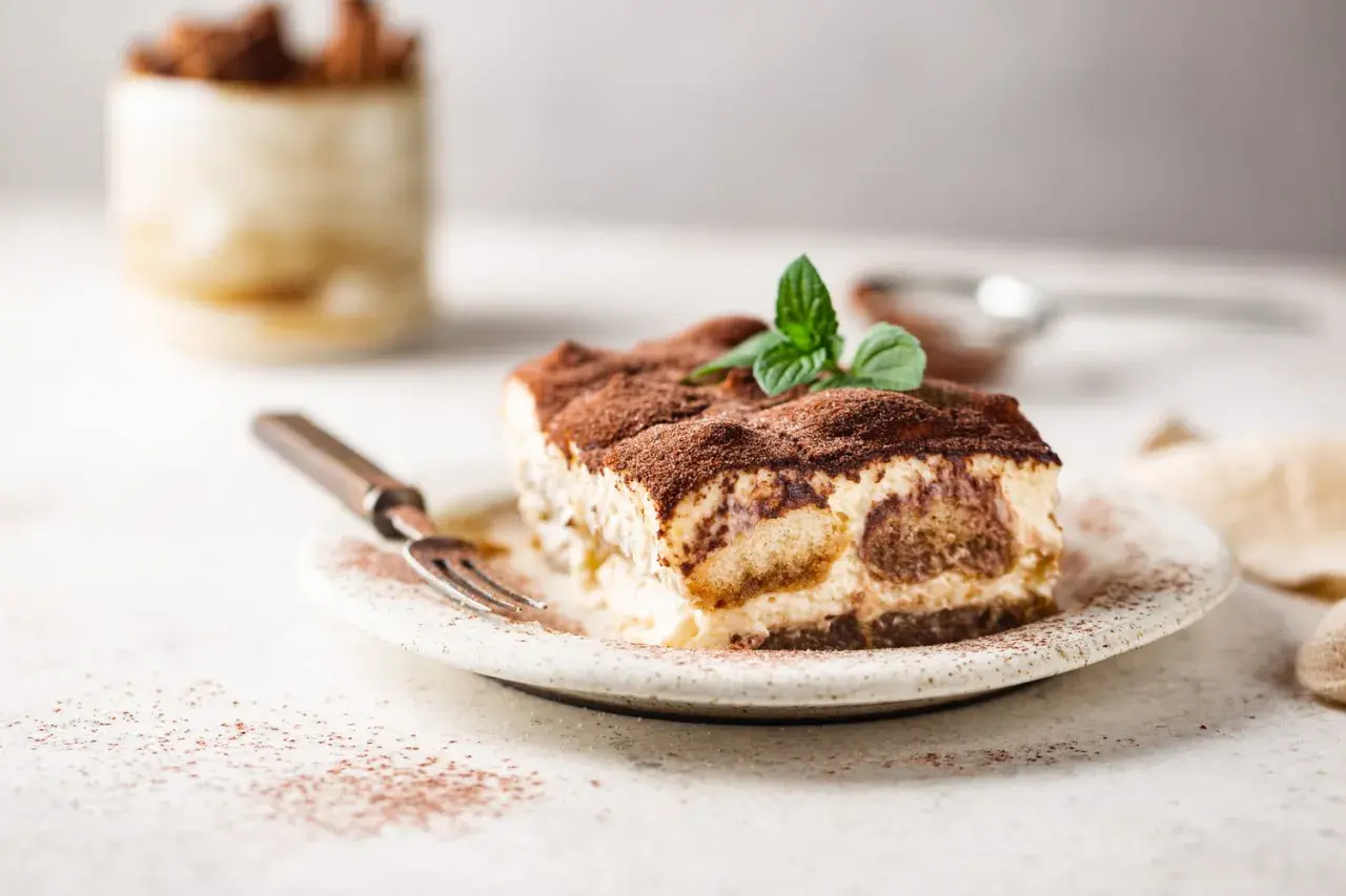 Une part de tiramisu onctueux, saupoudrée de cacao, garnie de menthe fraîche. Parfait pour une recette tiramisu réussie.
