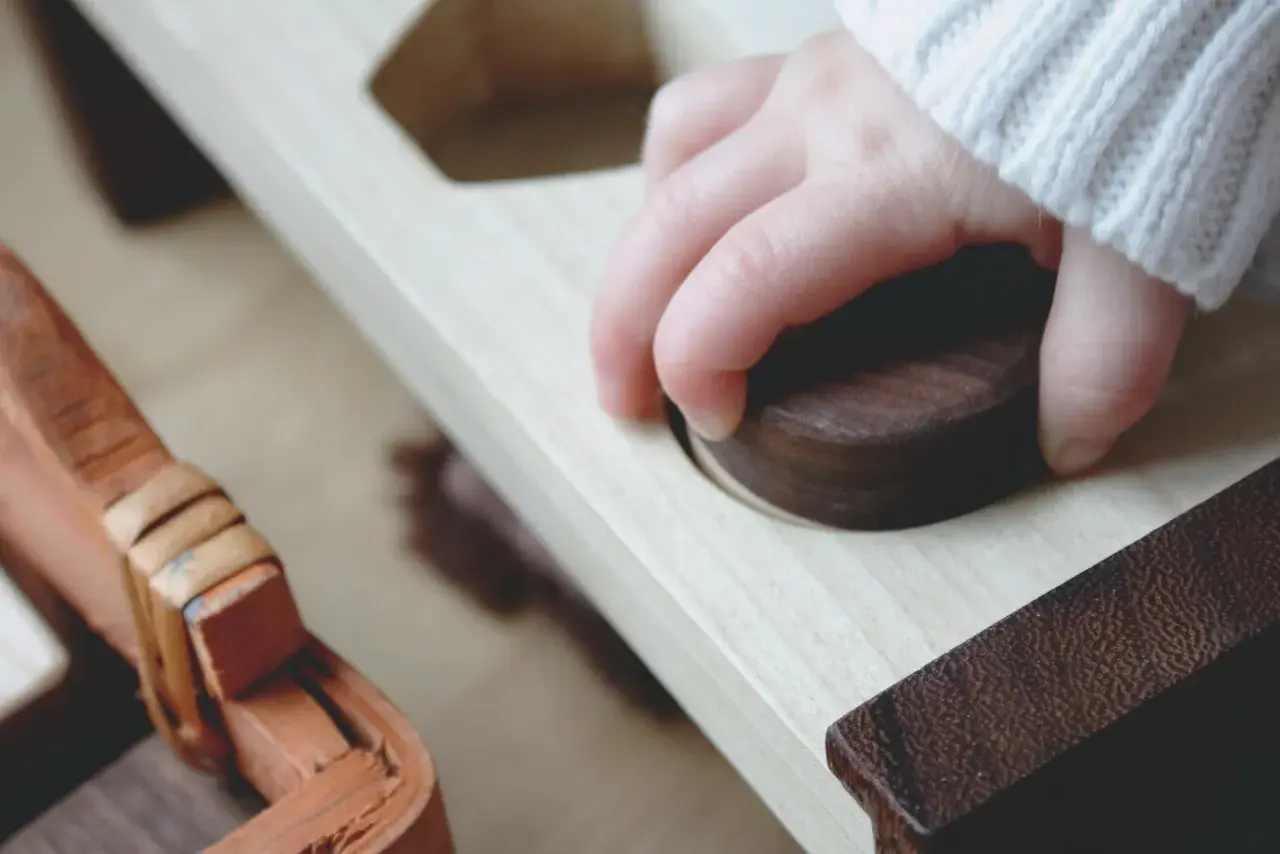 Mano de niño explorando un juguete de madera, un ejemplo del método Montessori para el desarrollo sensorial.