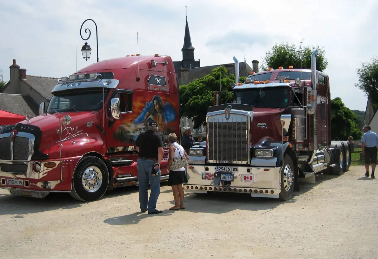 Deux camions américains tuning, l'un rouge vif avec une peinture personnalisée, l'autre bordeaux, se dressent fièrement.