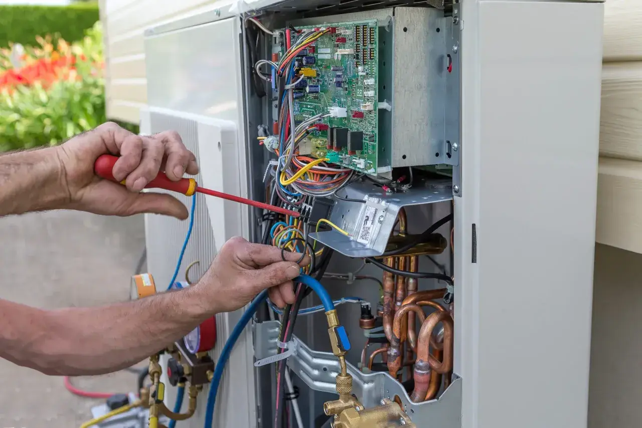 Fachowiec wykonuje serwis pomp ciepła Hitachi, pracując przy otwartej jednostce zewnętrznej z widoczną elektroniką i przewodami.