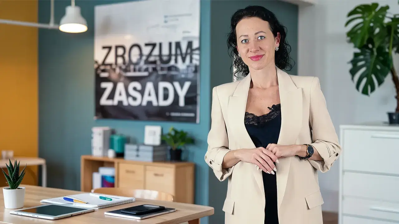 Kobieta w beżowej marynarce, obok niej na biurku leży tablet i notatnik, który może służyć jako księga przychodów i rozchodów.
