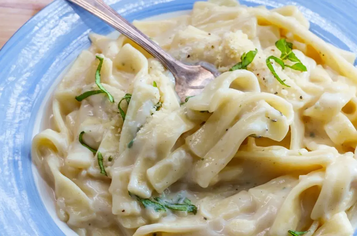 Pyszny makaron z tuńczykiem w sosie śmietanowo-serowym, udekorowany świeżą bazylią i parmezanem. Idealny na szybki obiad.