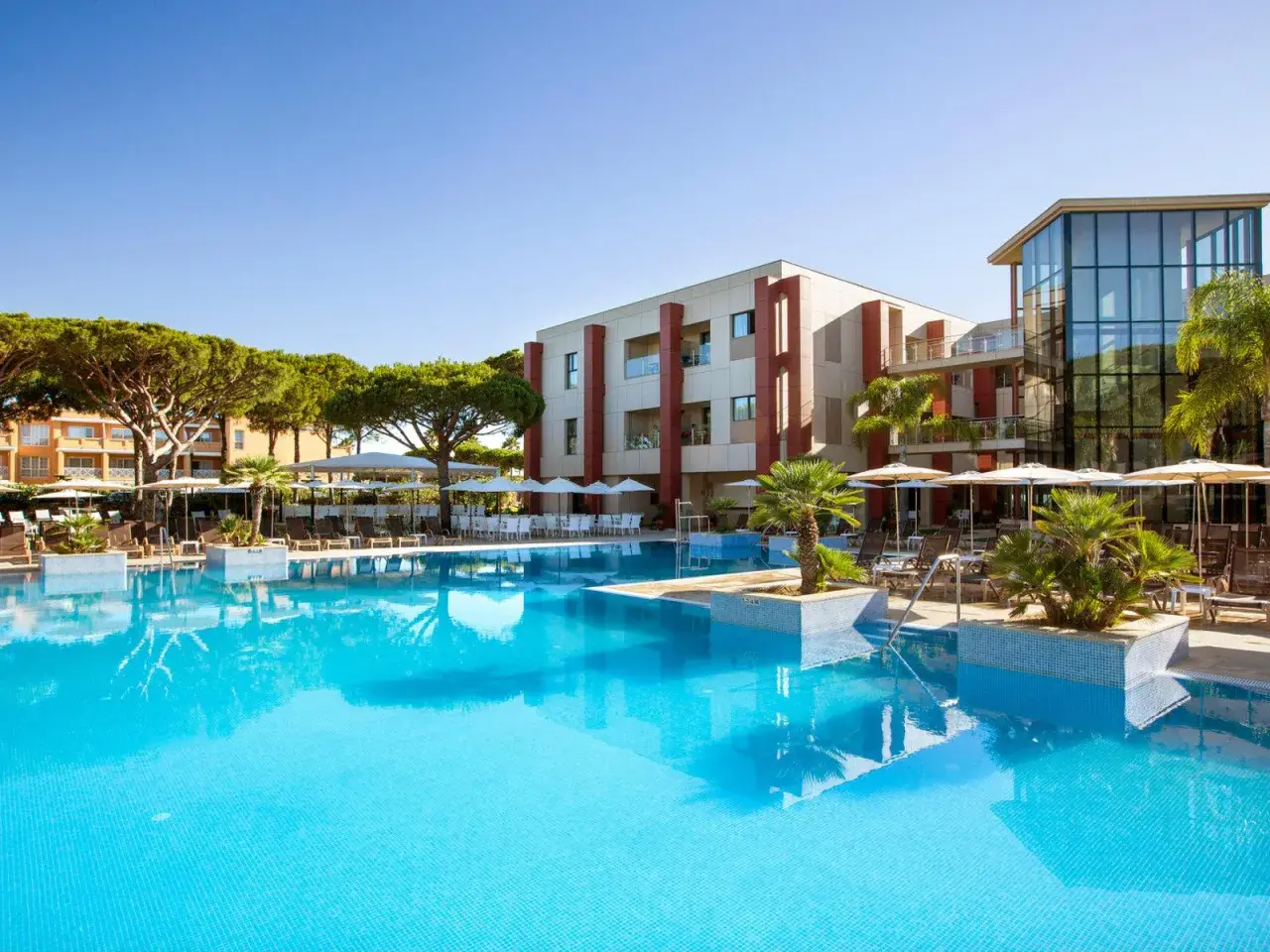 Einladender Poolbereich mit Palmen und Liegestühlen. Das Hotel mit moderner Architektur und dem TUI Kids Club Barrosa Garden verspricht einen tollen Urlaub.