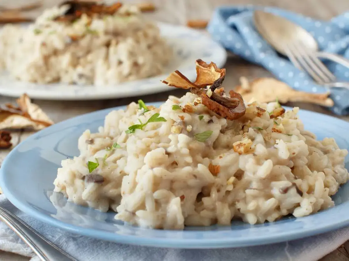 Delicioso risotto de setas cremoso, adornado con trozos de champiñones secos y nueces picadas, servido en un plato azul.
