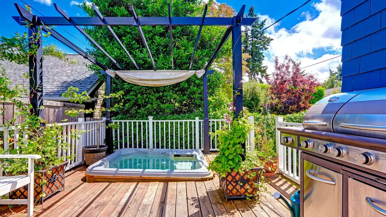 Un coin jacuzzi extérieur sous une pergola, avec un barbecue à proximité, invite à la détente.
