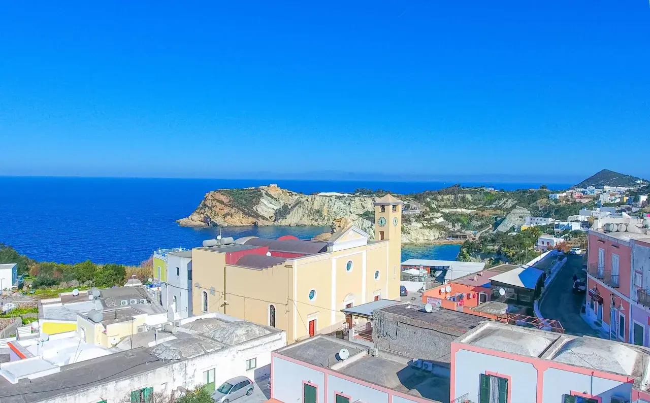 Vista panoramica dell'isola di Ponza con case colorate, una chiesa con campanile e il mare blu intenso.