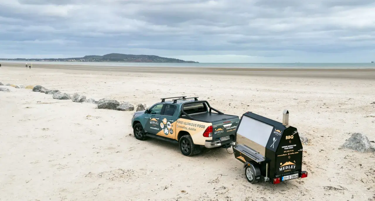 Un pick-up tracte un barbecue sur remorque sur une plage. Idéal pour fabriquer un barbecue sur remorque pour un événement en bord de mer.