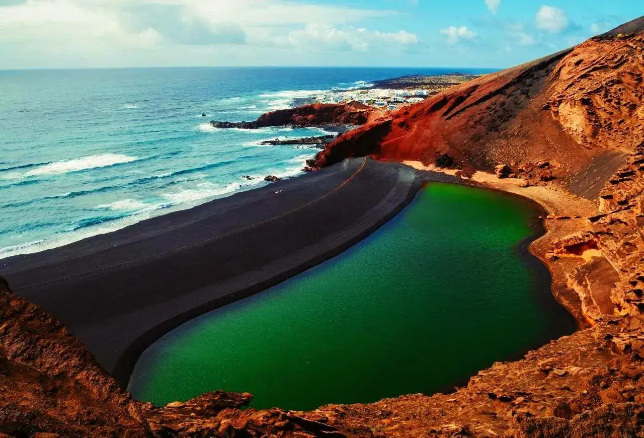 Zielona laguna otoczona czarną plażą i czerwonymi skałami. Niezwykłe miejsce, które warto zobaczyć na Lanzarote.
