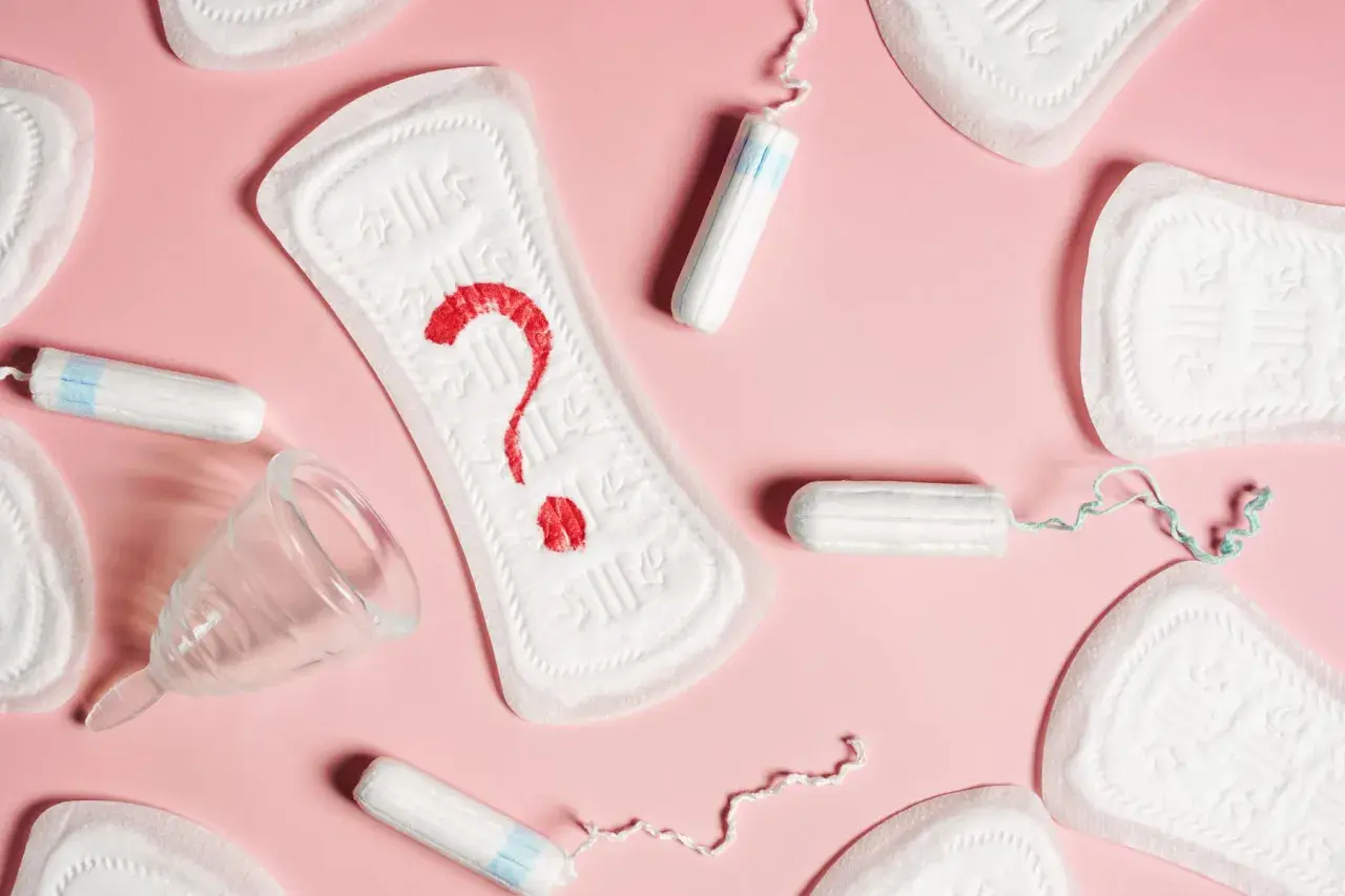 Plamienie 3 dni po okresie? Podpaski, tampony i kubeczek menstruacyjny na różowym tle.
