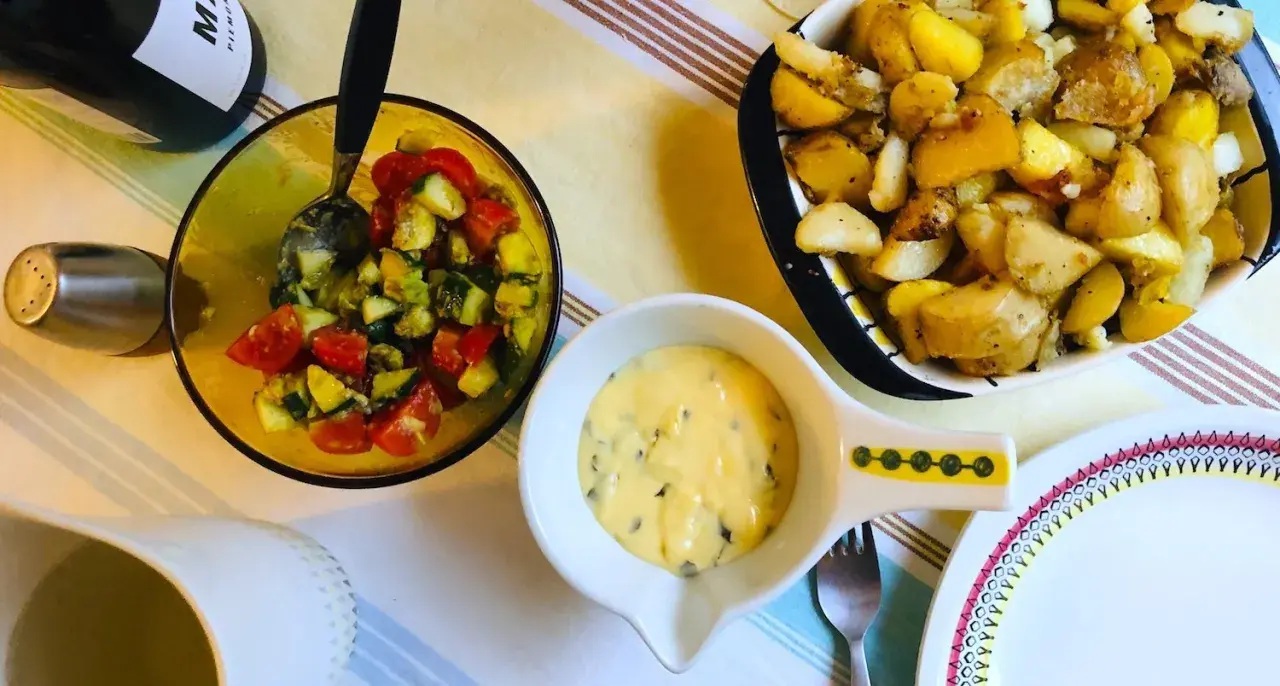 En skål med bearnaisesås recept, bredvid en sallad med tomat och gurka samt ugnsrostade potatisar.