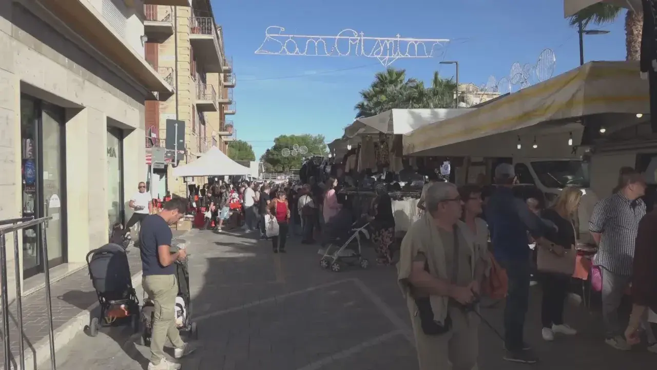 Festa San Crispino a Porto Sant'Elpidio: bancarelle affollate, gente che passeggia e acquista sotto un cielo azzurro.