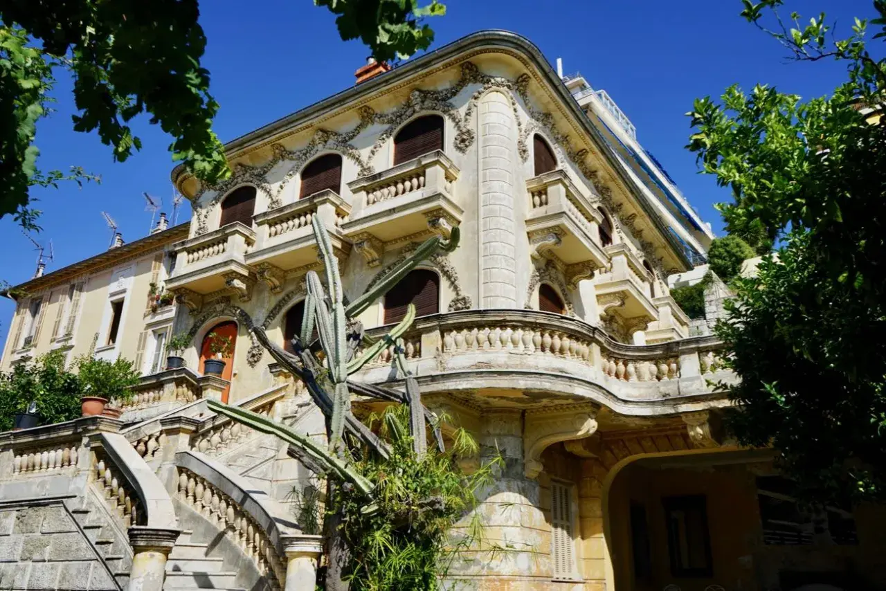 Élégante villa abandonnée sur la Côte d'Azur, avec un grand escalier en pierre et un cactus imposant devant sa façade ornée.
