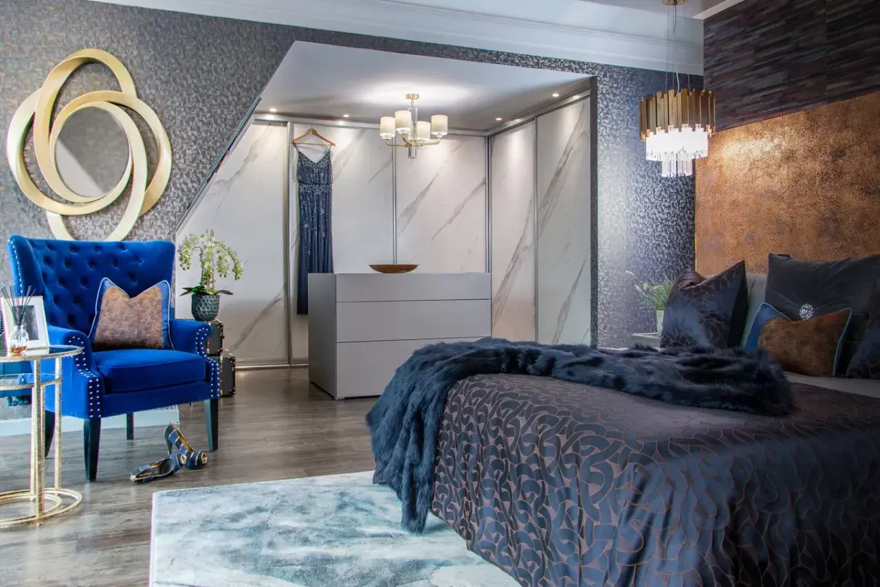 Luxurious bedroom with a king bed styled with dark blue bedding and a faux fur throw. A plush blue armchair and gold accents complete the opulent look.