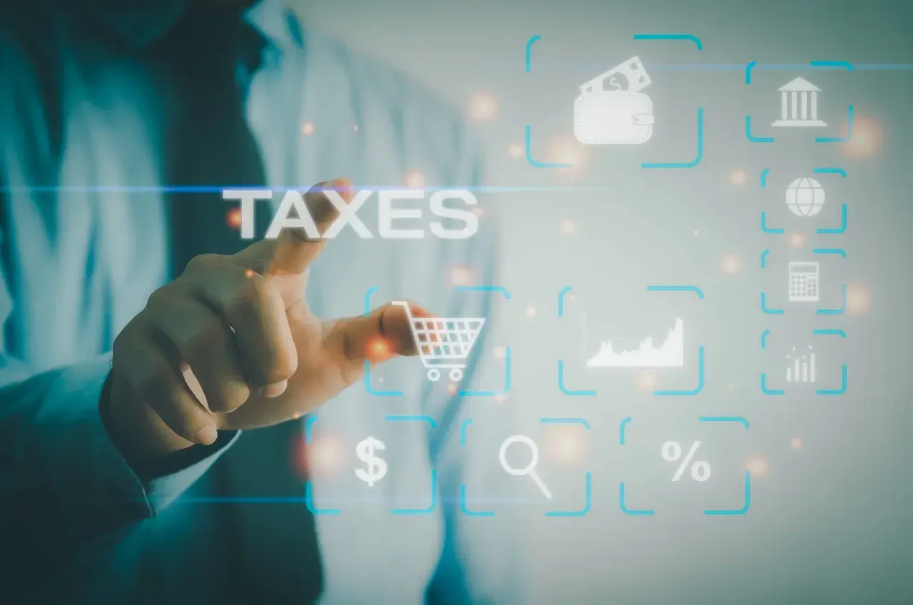 Dłoń dotyka ekranu z napisem TAXES. Wokół ikony symbolizujące finanse, handel i analizę danych, jak koszyk, portfel, wykresy, lupa, procent, kalkulator, bank i globus. To cyfrowy świat zarządzania podatkami, gdzie każdy element ma swoje znaczenie w sys...