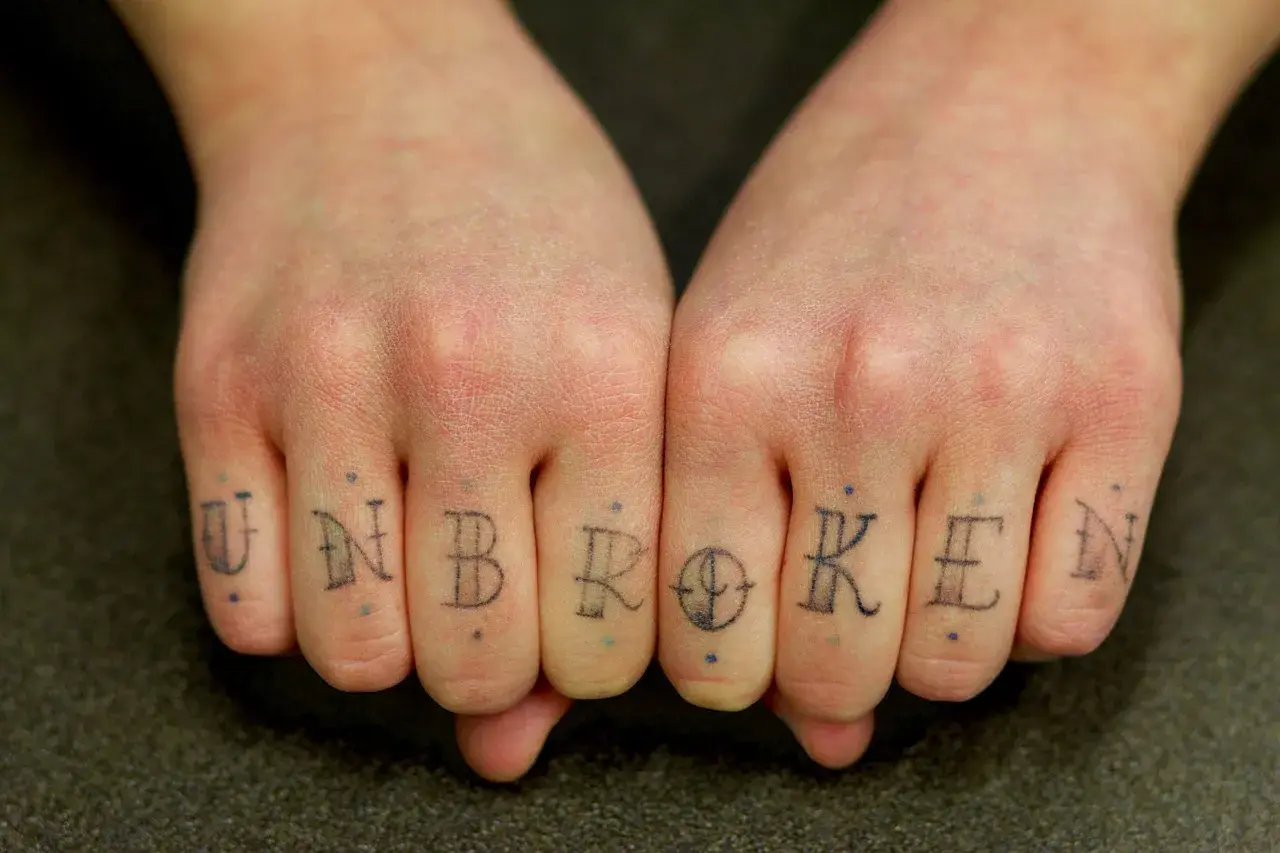 Tatuaż na palcach tworzy napis "UNBROKEN". To jak trwały pierścionek, symbol siły.