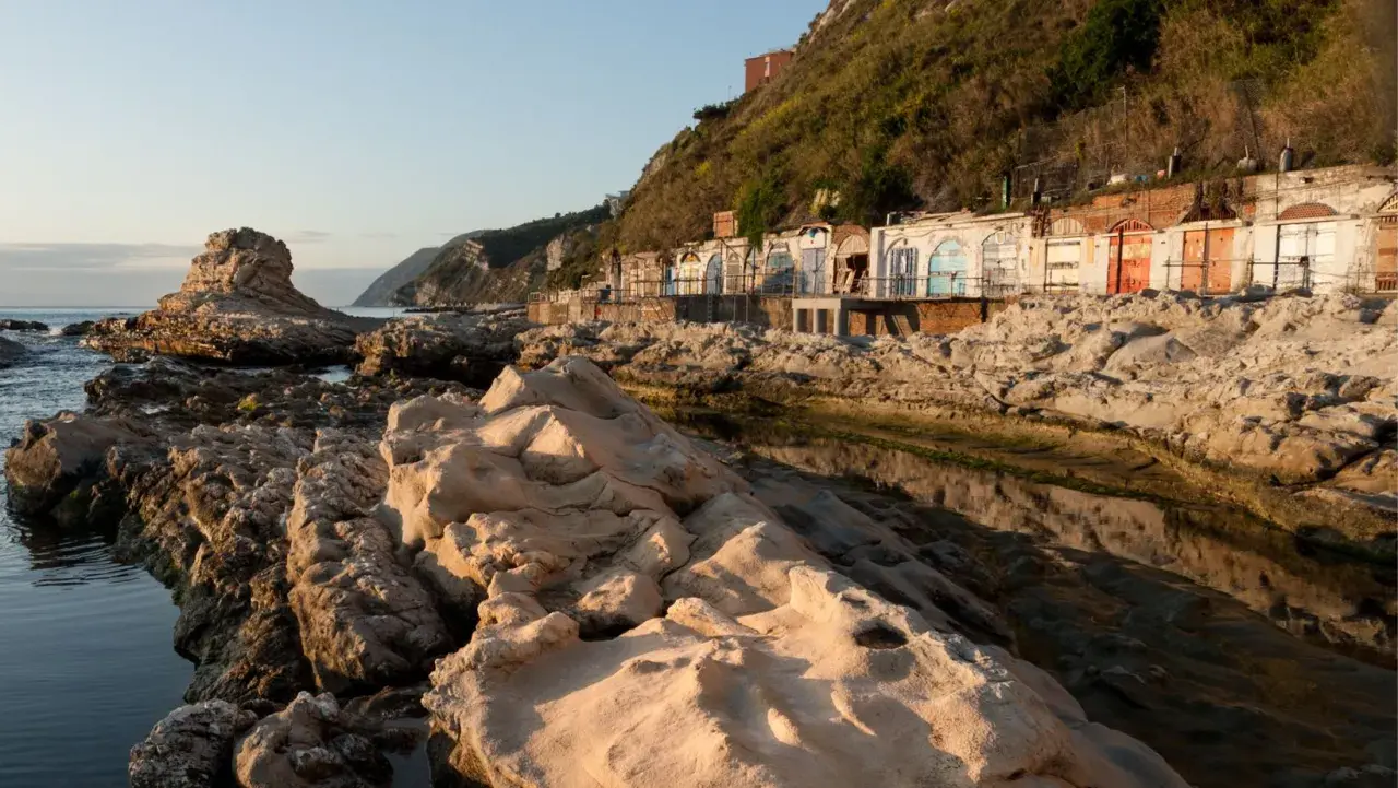 Scogliere rocciose e cabine colorate sulla spiaggia del Passetto, illuminate dalla luce dorata del tramonto.