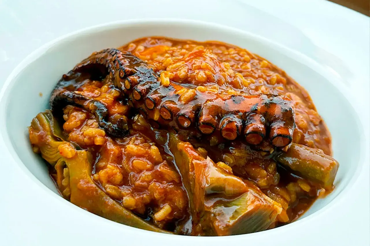 Delicioso arroz con pulpo y trozos de alcachofa en un cuenco blanco.