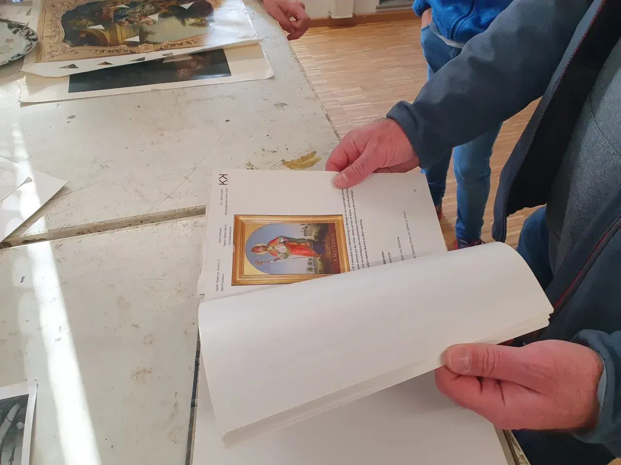 Hände halten ein Buch mit einem Bild eines Heiligen. Ein Detail der Kunstrestauration.