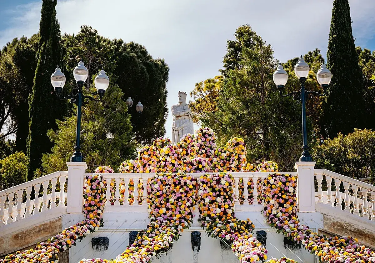 Escaleras adornadas con miles de flores vibrantes, donde zgz florece en un espectáculo de color. Una estatua real preside la escena.