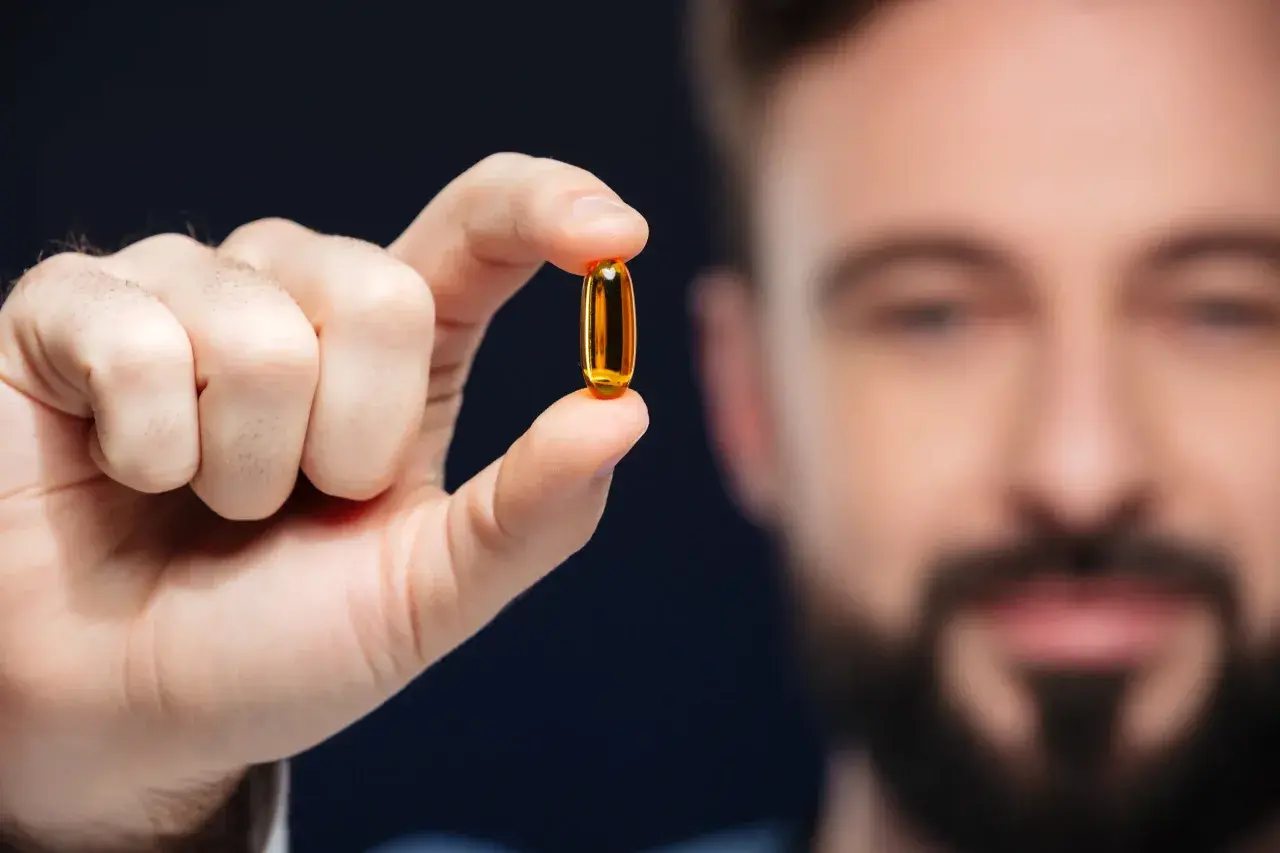 Mężczyzna trzyma kapsułkę z olejem rybim, bogatym w kwasy omega 3.