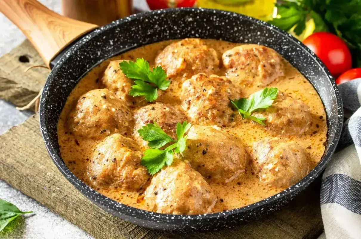 Pulpeciki w kremowym sosie, udekorowane natką pietruszki, gotowe do podania. Pyszny sos do pulpetów kusi aromatem.