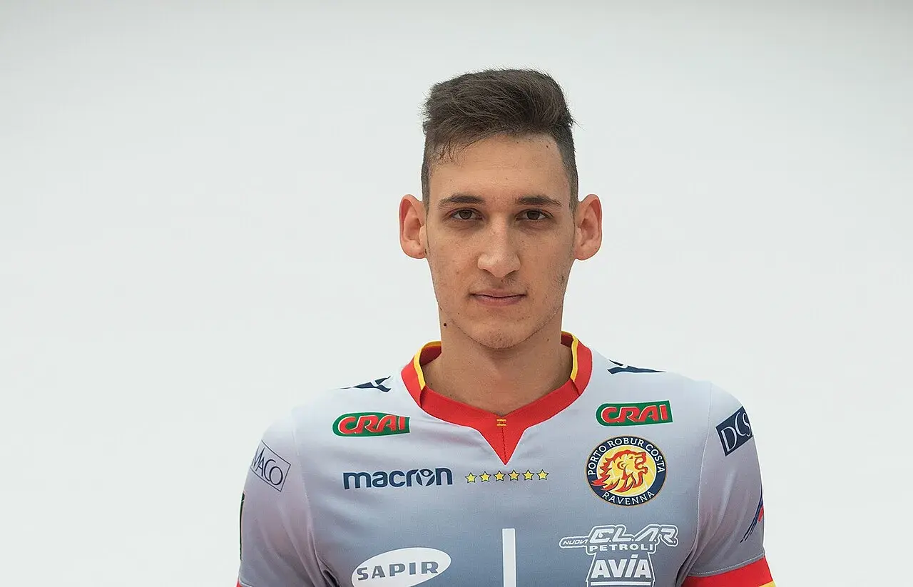 Młody siatkarz z krótką fryzurą, ubrany w szary strój z logo Porto Robur Costa Ravenna.