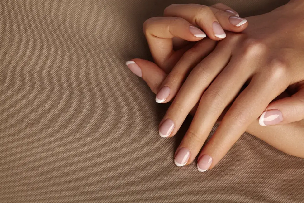 Dłonie z idealnym frenczem, podkreślającym naturalne kolory paznokci. Delikatny manicure na beżowym tle.