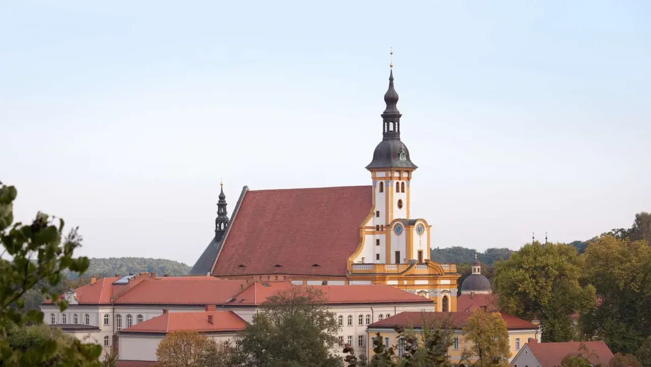 Das Kloster Neuzelle mit seinen roten Dächern und dem markanten Turm, umgeben von Bäumen.