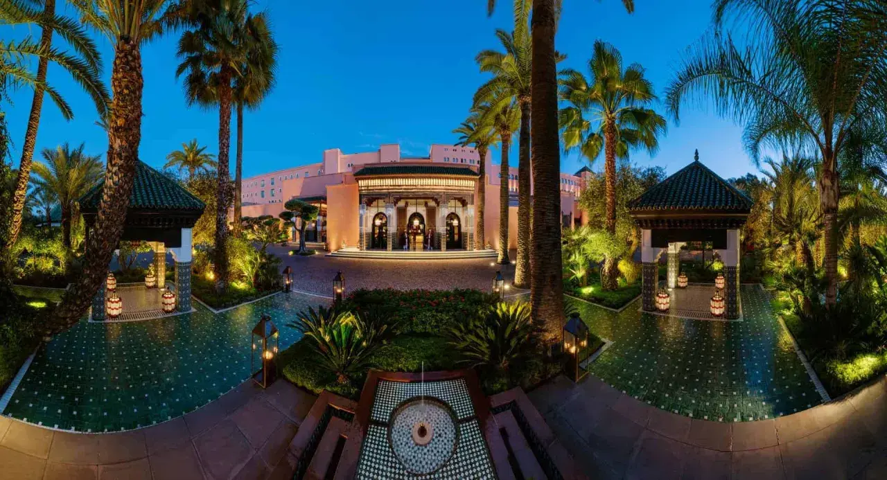 Eingangsbereich des La Mamounia Hotels in Marrakesch bei Dämmerung, umgeben von Palmen und beleuchteten Pavillons.