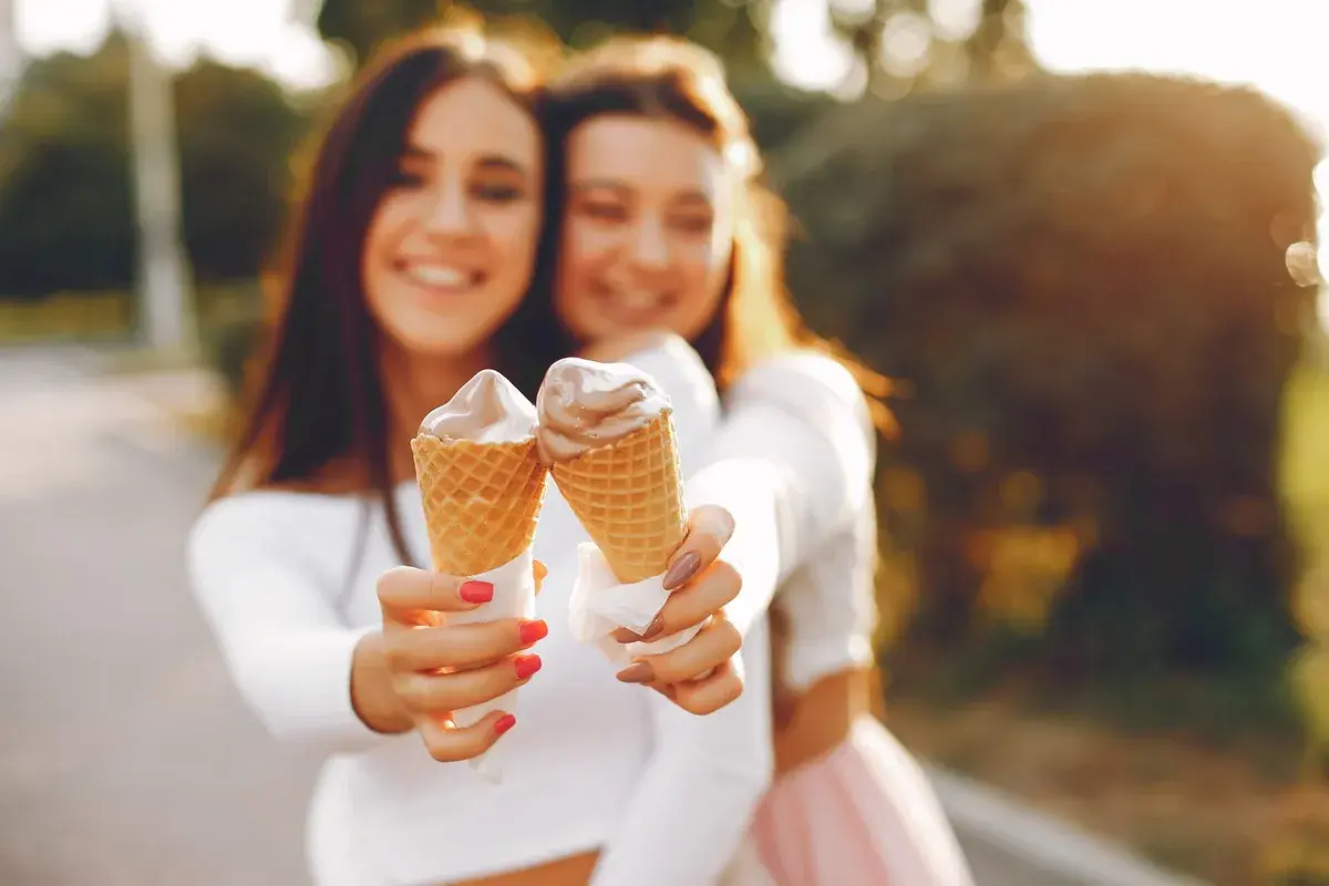 Dwie uśmiechnięte dziewczyny trzymają lody w wafelkach. Czy lody tuczą? Może odrobina przyjemności nie zaszkodzi!