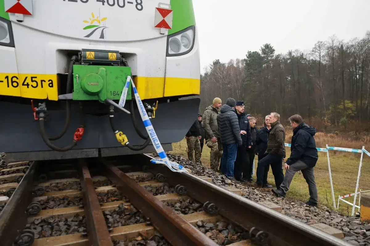Grupa osób, w tym policjanci, ogląda przód lokomotywy EU07 005, otoczony taśmą policyjną.
