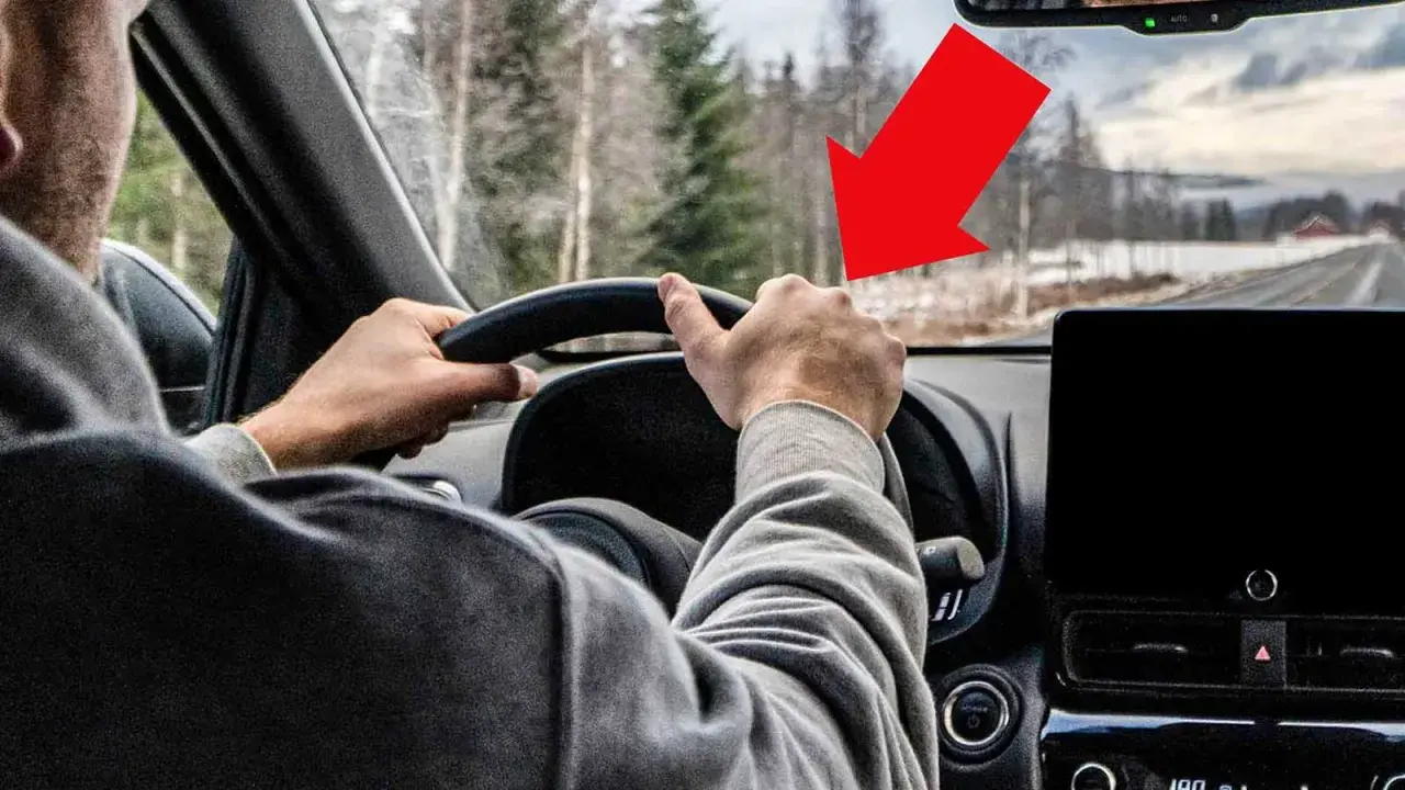 Förarens händer på ratten, en röd pil pekar mot vägen där det kan finnas vibrationer i bilen.