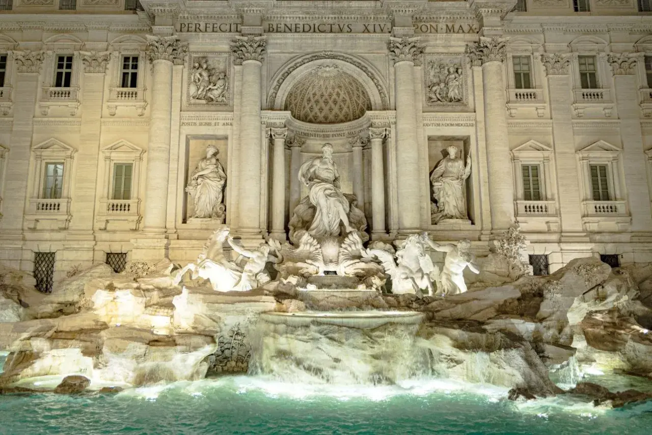 Trevi Fountain at night, with illuminated sculptures and cascading water.