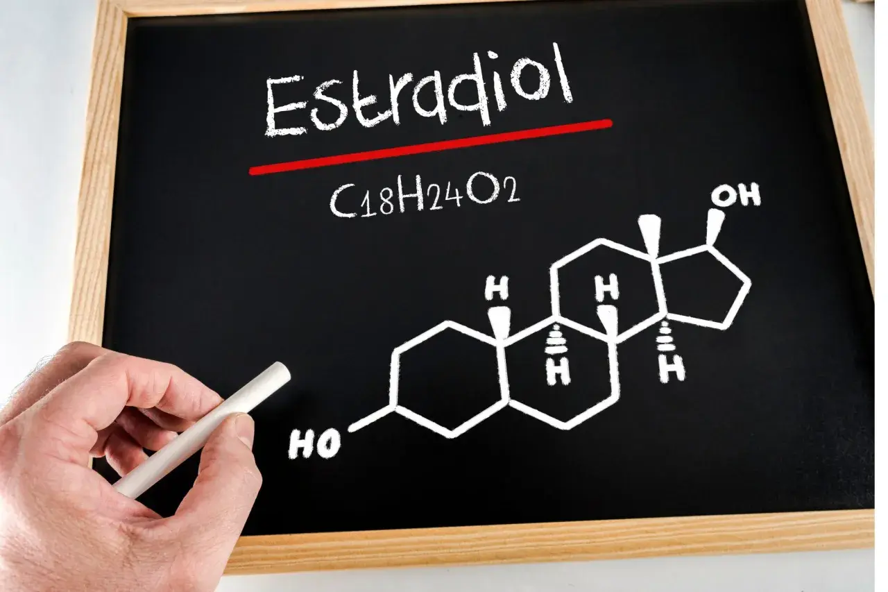 Tablica z napisem "Estradiol" i jego wzorem chemicznym C18H24O2. Dłoń trzyma kreda.
